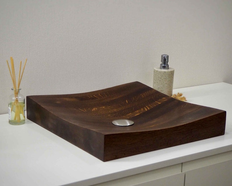 Peut inclure: Un &eacute;vier en bois brun fonc&eacute; avec un design incurv&eacute; et un drain argent&eacute;. L'&eacute;vier est pos&eacute; sur un comptoir blanc.