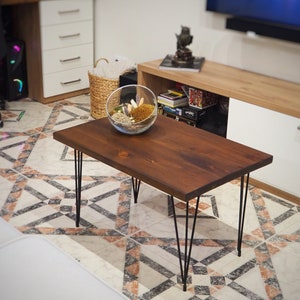 May include: A dark brown wooden coffee table, approx. 120 cm long, with black hairpin legs. A glass terrarium with decorative elements sits on the table. The table is in a living room setting.