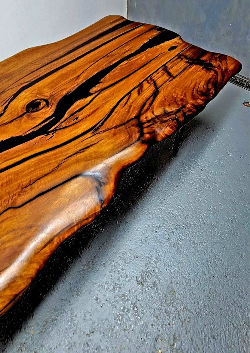 May include: A large, live edge coffee table with a natural wood top and black epoxy resin filling the cracks and knots. The table has a rustic, organic look.
