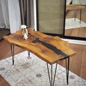 May include: A wooden coffee table with a black epoxy resin inlay and hairpin legs. The table is on a patterned rug.