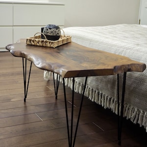 May include: A wooden coffee table with a live edge top and black hairpin legs. The table is made of natural wood and has a rustic look. The table is sitting on a hardwood floor.