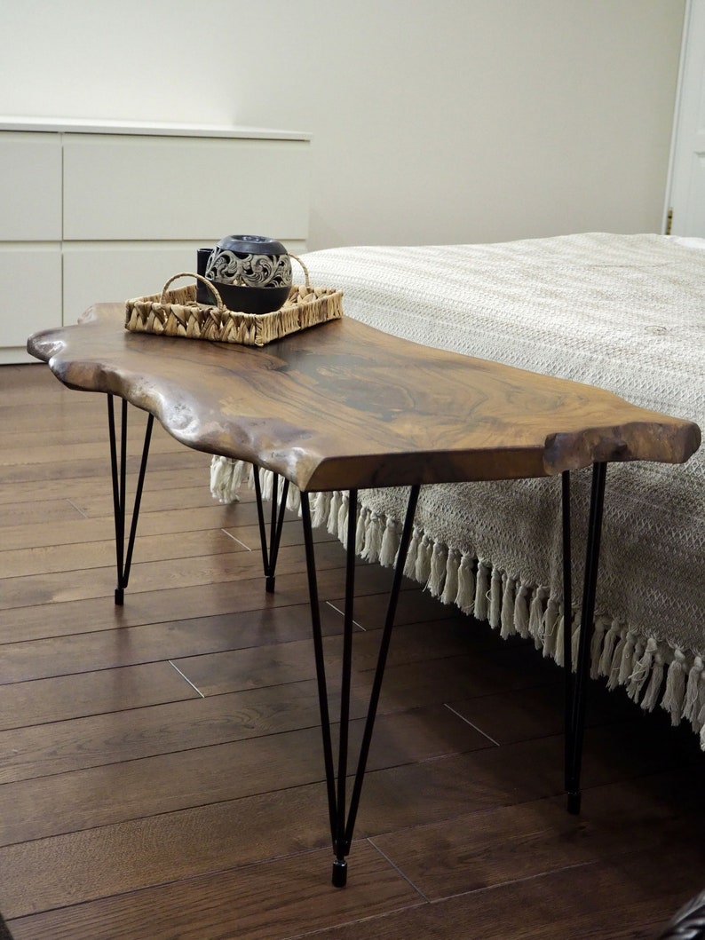 May include: A wooden coffee table with a live edge top and black hairpin legs. The table is made of natural wood and has a rustic look. The table is sitting on a hardwood floor.