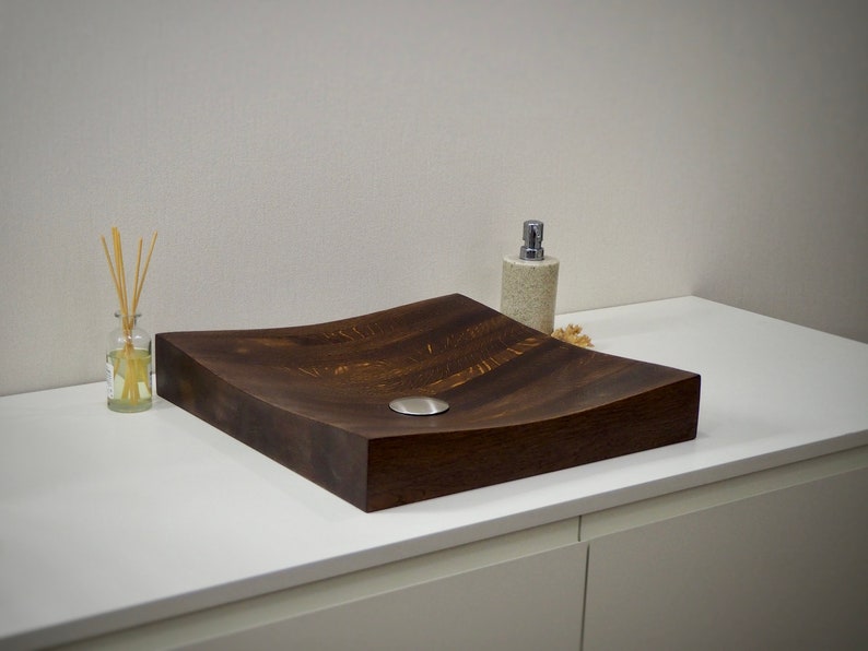 Peut inclure: Un &eacute;vier en bois brun fonc&eacute; avec un design incurv&eacute; et un drain en acier inoxydable. L'&eacute;vier est pos&eacute; sur un comptoir blanc.