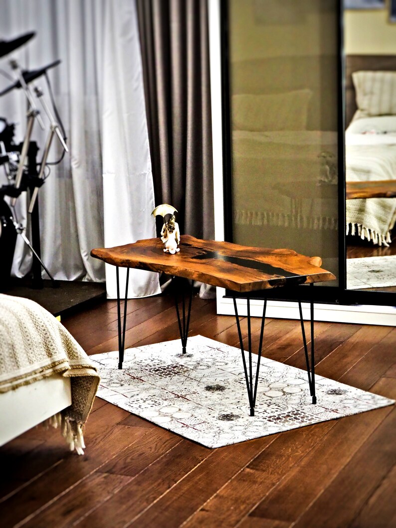May include: A wooden coffee table with a live edge top and black epoxy resin inlay. The table has black hairpin legs and is sitting on a white and red patterned rug.