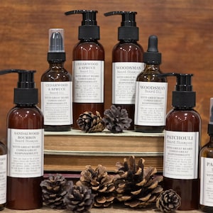 Puede incluir: Una variedad de botellas de vidrio marrón con bombas y pulverizadores negros, etiquetadas con textos como "Sandalwood Bourbon" y "Cedarwood & Spruce". Las botellas están dispuestas con piñas sobre una superficie de madera.