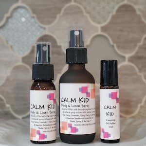 May include: Three bottles of essential oil blends labelled "Calm Kid" in a calming colour scheme of pink, blue, and white. The bottles are a spray bottle, a roll-on bottle, and a smaller spray bottle. The text on the bottles reads "Calm Kid Body & Linen Spray" and "Calm Kid Essential Oil Roller 10ml".