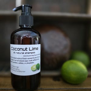 May include: A dark amber plastic bottle with a black pump dispenser containing Coconut Lime all natural shampoo. The white label features the product name, a URL, descriptive text about the ingredients, and an image of two green limes.