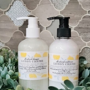 May include: Two white bottles with pumps, one labelled "all natural shampoo LEMON CREME" and the other labelled "all natural conditioner LEMON CREME". Both bottles are surrounded by green foliage.