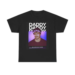 Puede incluir: Camiseta negra con un gráfico de un hombre con una corona de flores. La palabra "DADDY" se repite encima de la imagen, con la frase "IS A STATE OF MIND" debajo.