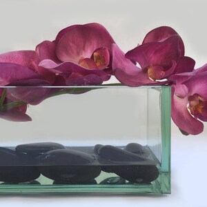 May include: A glass vase filled with water and black stones, with a cluster of pink orchids floating on top.