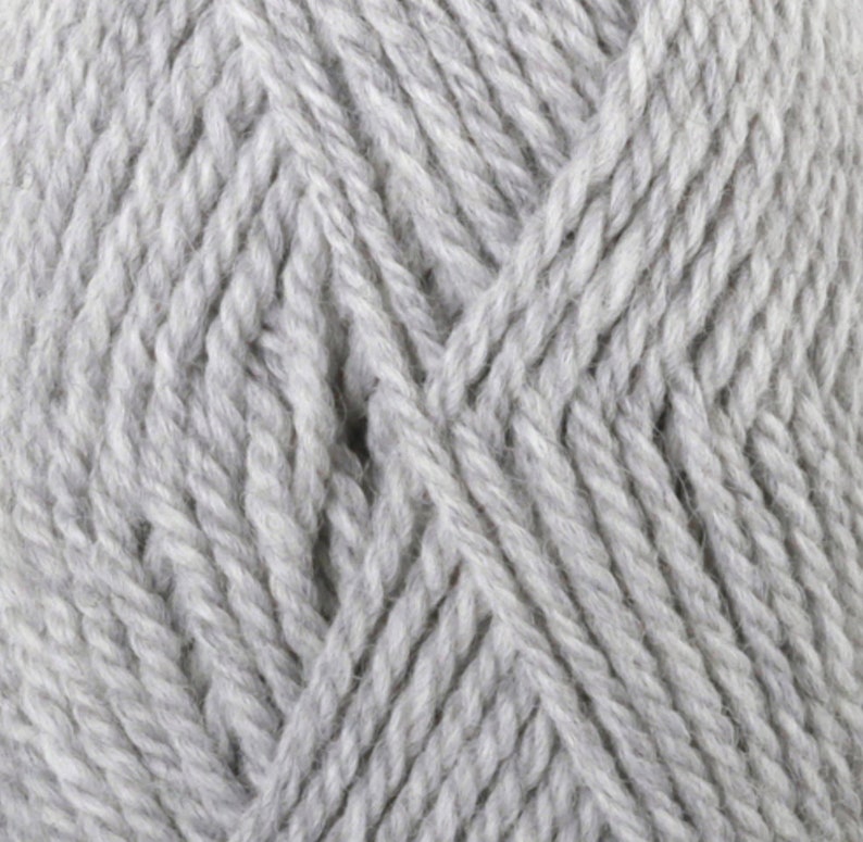 May include: Close-up of a skein of light gray yarn. The yarn is tightly twisted, showing a textured surface. The fibers are thick and appear soft, suitable for knitting or crocheting projects. The color is a neutral, versatile shade.