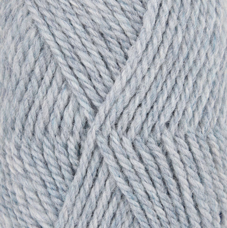 May include: Close-up of a skein of light blue yarn. The yarn has a textured appearance with visible fibers and a slight marled effect. The yarn is tightly wound, showing the individual strands. Ideal for knitting and crochet projects.