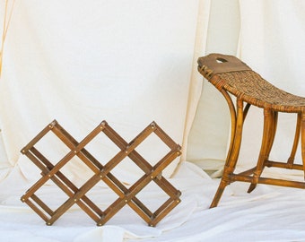 May include: A wooden wine rack with a woven rattan bench in front of a white backdrop.