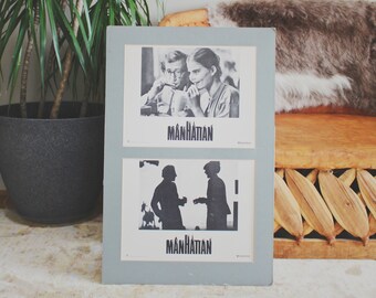 Op de afbeelding: Een vintage filmposter voor de film "Manhattan" met twee zwart-wit afbeeldingen. De bovenste afbeelding toont een stel dat naar elkaar kijkt. De onderste afbeelding toont twee silhouetten van mensen die lopen.