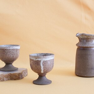 May include: Two brown and white ceramic cups with a pedestal base and a brown and white ceramic pitcher with a handle.