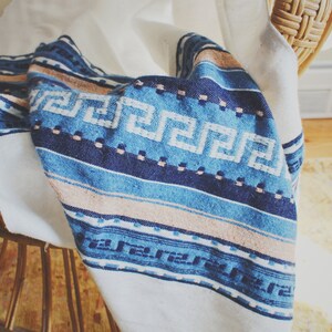 May include: A white blanket with a blue and pink patterned design. The blanket is draped over a wooden chair.