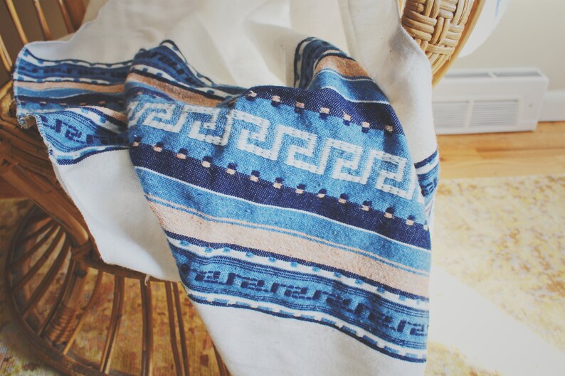 May include: A white blanket with a blue and pink patterned design. The blanket is draped over a wooden chair.