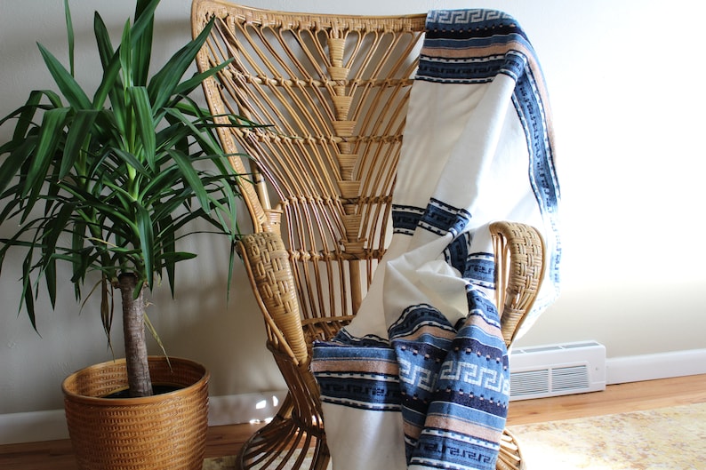 May include: A woven wicker chair with a white and blue patterned throw blanket draped over it. The chair has a unique, open design with a wide, rounded back.