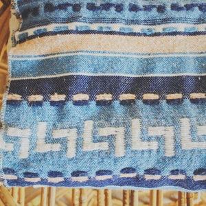 May include: A blue and white striped throw blanket with a geometric pattern. The blanket is woven with a fringe border and has a subtle texture.