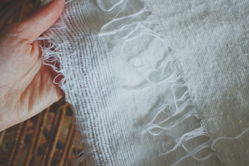 May include: A white fabric with a frayed edge. The fabric has a woven texture and is slightly wrinkled.