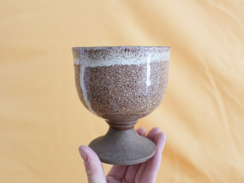 May include: A brown and white ceramic goblet with a speckled glaze. The goblet has a wide base and a rounded bowl.