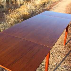 Puede incluir: Una mesa de comedor extensible de madera con un acabado marr&oacute;n oscuro. La mesa tiene una tapa rectangular y cuatro patas. La mesa se muestra en un entorno des&eacute;rtico.