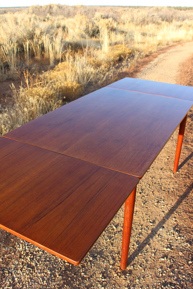 Puede incluir: Una mesa de comedor extensible de madera con un acabado marr&oacute;n oscuro. La mesa tiene una tapa rectangular y cuatro patas. La mesa se muestra en un entorno des&eacute;rtico.