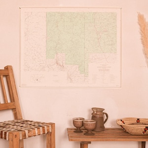 May include: A wooden chair with a woven seat sits next to a small wooden table with two glasses, a ceramic jug, and a woven basket. A map hangs on the wall behind the chair. A bouquet of dried pampas grass stands in a vase on the right side of the image.
