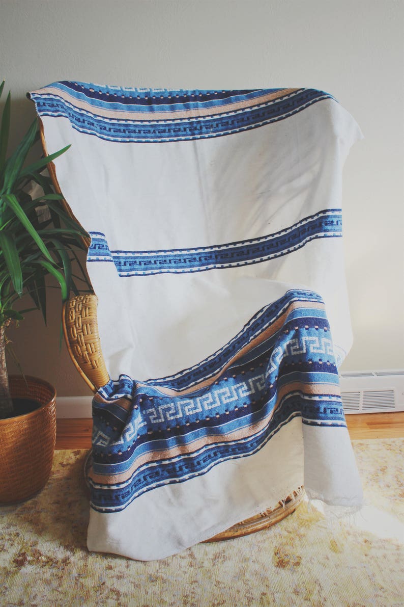 May include: A white throw blanket with blue and pink stripes and a geometric pattern. The blanket is draped over a wicker chair.