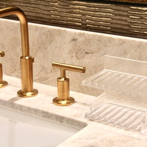 May include: Gold bathroom faucet with a single lever handle and a clear plastic soap dish with two compartments. The faucet is labeled "Kohler".