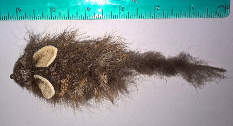 May include: A brown and white furry toy mouse with a long tail. The toy is designed to look like a real mouse.