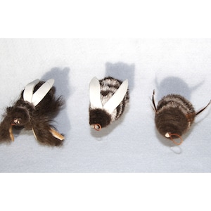 May include: Three plush bumblebees with black and white striped bodies and white wings. The bumblebees are made of soft, fuzzy material and have a wire loop for hanging.
