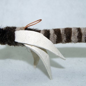 Może przedstawiać: Pluszowa zabawka w brązowo-białe paski z białymi skrzydłami i miedzianymi antenami z drutu. Zabawka jest zaprojektowana tak, aby przypominała muchę.