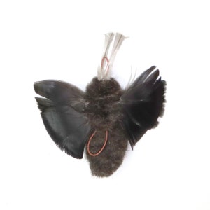 May include: A small, black, fluffy, bird-shaped ornament with wings made of feathers. The ornament has a copper wire loop at the top for hanging.