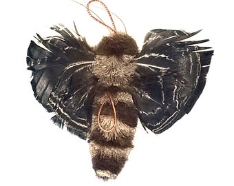 May include: A brown and black fuzzy moth with black and white feathered wings. The moth has a red string attached to its head.