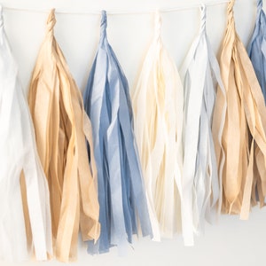 Puede incluir: Una guirnalda de borlas de papel de seda en blanco, beige y azul.