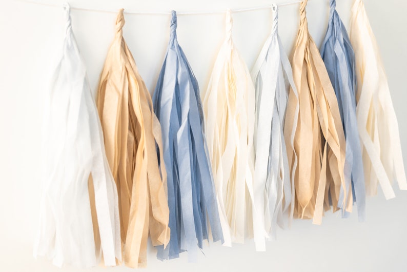 Puede incluir: Una guirnalda de borlas de papel de seda en blanco, beige y azul.