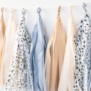 May include: A garland of tissue paper tassels in beige, blue, and white with a black and white polka dot pattern.