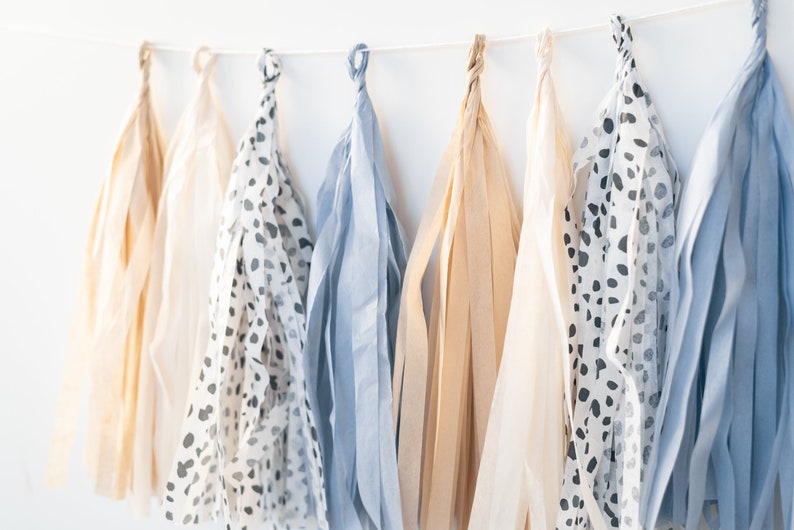 May include: A garland of tissue paper tassels in beige, blue, and white with a black and white polka dot pattern.
