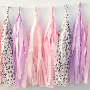 Puede incluir: Una guirnalda de borlas de papel de seda en rosa y morado con un estampado de animales en blanco y negro. Las borlas est&aacute;n enhebradas con una cuerda blanca.