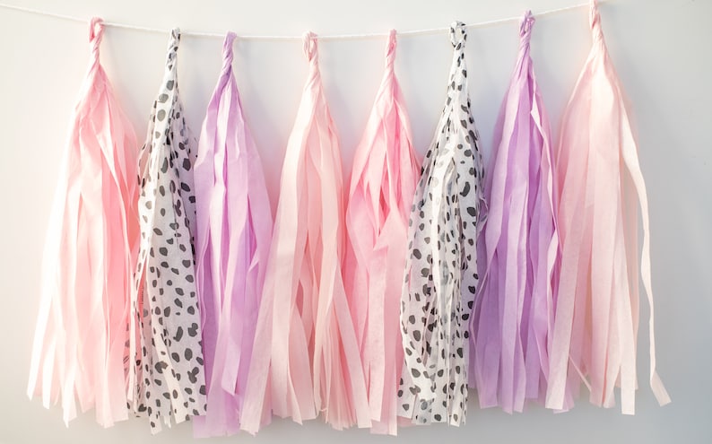 Puede incluir: Una guirnalda de borlas de papel de seda en rosa y morado con un estampado de animales en blanco y negro. Las borlas est&aacute;n enhebradas con una cuerda blanca.