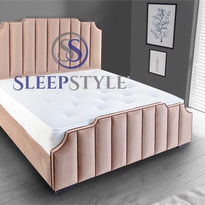 May include: A light pink upholstered bed frame with a tufted headboard and a white mattress. The headboard has a curved top and a logo that says "SLEEPSTYLE".