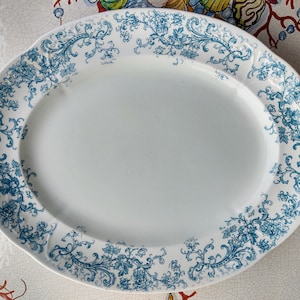 May include: Oval white serving platter with a blue floral design around the rim. The platter has a slightly raised edge and is suitable for serving food. The floral pattern includes flowers and leaves.