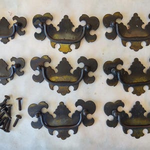 May include: Eight ornate metal drawer pulls with a decorative design and a black finish. The pulls are arranged in two rows of four. There are also several screws included.