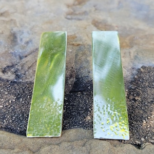 May include: A pair of silver rectangular earrings with a hammered texture. The earrings are on a gray textured surface.
