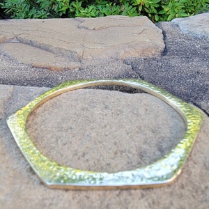 May include: A gold hexagon-shaped bangle bracelet with a hammered texture.
