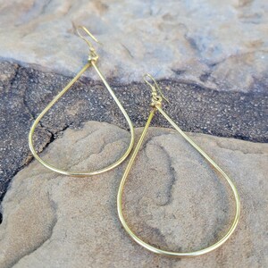 May include: A pair of gold teardrop shaped earrings. The earrings are made of a thin wire and have a simple, minimalist design.