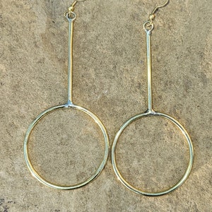 May include: A pair of gold-toned earrings with long, thin, straight posts and circular hoops at the bottom.
