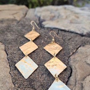 May include: Gold-toned earrings with a hammered finish. Each earring features three diamond-shaped pendants.