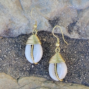 May include: A pair of gold earrings with white cowrie shells. The shells are wrapped in gold wire and the earrings have a simple drop design.